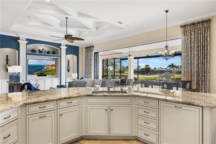 Kitchen featuring ceiling fan with notable chandelier, sink, coffered ceiling, crown molding, and light stone countertops