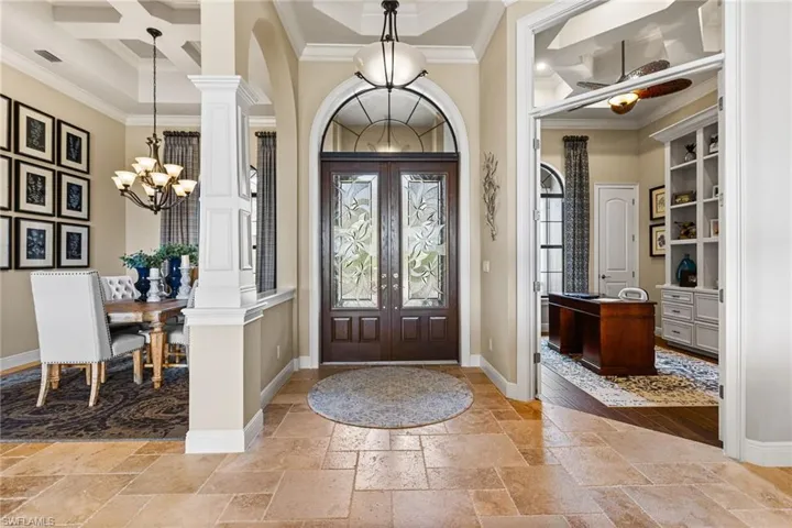 Foyer entrance with ornate columns, coffered ceiling, crown molding, an inviting chandelier, and french doors