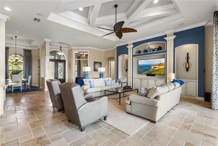 Living room with crown molding, coffered ceiling, ceiling fan with notable chandelier, and beam ceiling