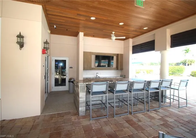 View of patio featuring an outdoor kitchen, ceiling fan, and a bar