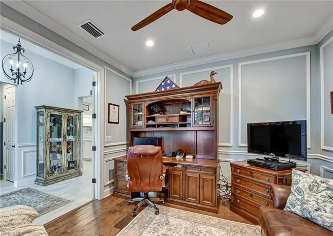Office area with ceiling fan with notable chandelier, hardwood / wood-style floors, built in desk, and crown molding