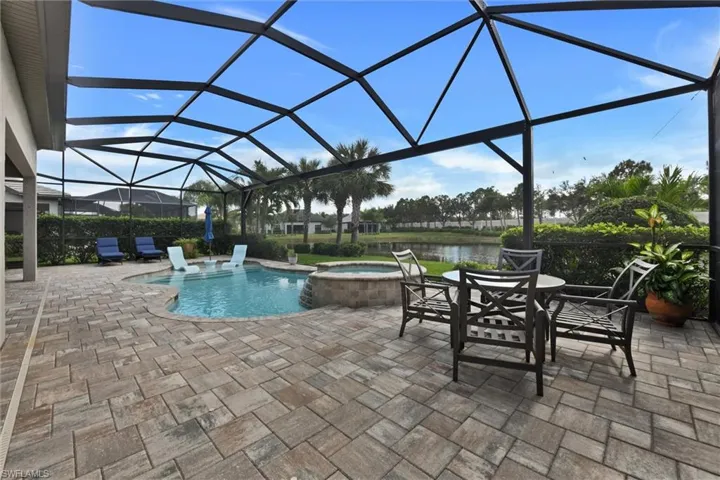 View of pool featuring a patio, a water view, a lanai, and an in ground hot tub