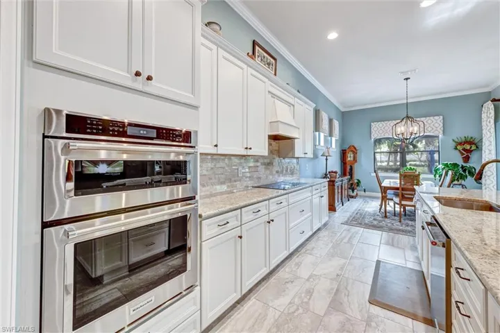 Kitchen with stainless steel appliances, light stone countertops, an inviting chandelier, sink, and white cabinets