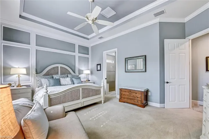 Bedroom with light colored carpet, connected bathroom, ceiling fan, a raised ceiling, and crown molding
