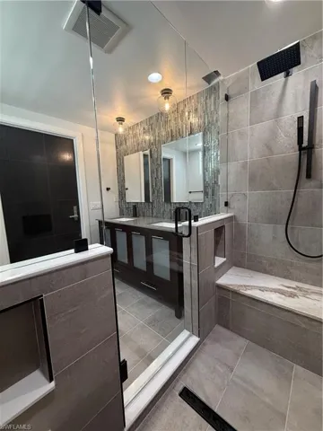 Full bathroom with double vanity, light tile patterned flooring, tiled shower, and tile walls