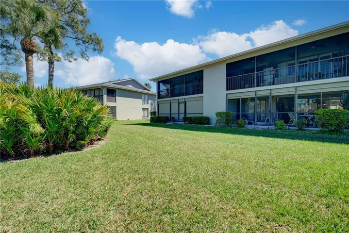View of green lawn featuring a sunroom and a balcony