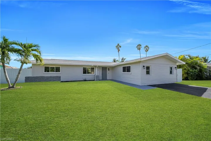 Single-story exterior featuring light-toned horizontal siding, a multi-paneled roofline, integrated wall-mounted lighting, and an asphalt driveway