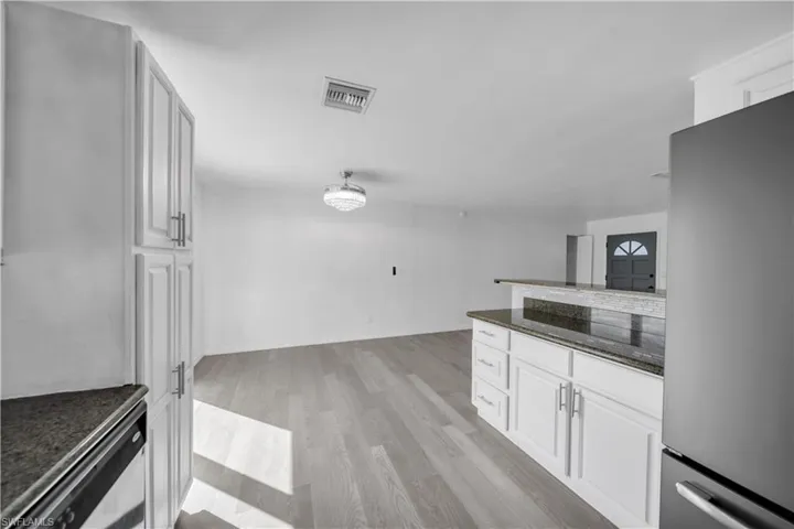 Kitchen featuring white shaker-style cabinetry, dark stone countertops, wood-finish flooring, and a crystal-style flush mount ceiling light