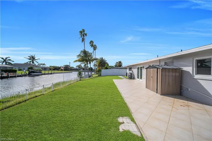 Waterfront backyard featuring a manicured lawn, tiled patio, and perimeter fencing