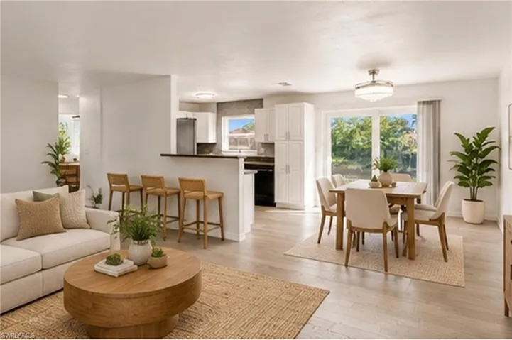 Open-concept interior featuring wood-finish flooring, white shaker-style cabinetry, breakfast bar, and sliding glass doors