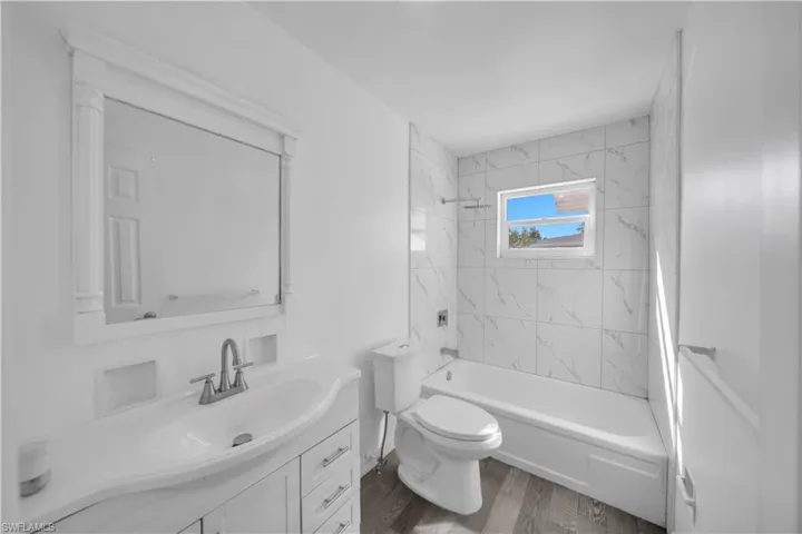 Bathroom featuring a white vanity with an integrated basin, framed wall mirror, tub-shower combination with full-height tile surround, and wood-finish flooring