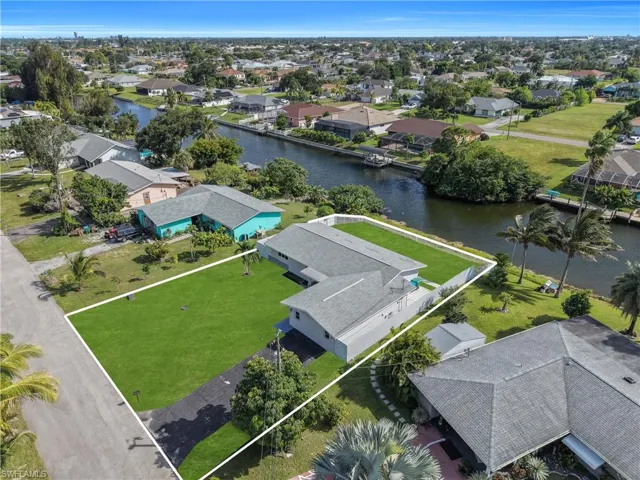 Waterfront property featuring direct canal access, expansive lawn, paved driveway, and perimeter fencing