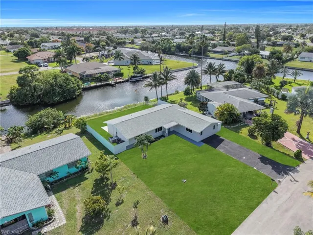 Waterfront property featuring a canal-side bulkhead, expansive lawn, asphalt driveway, and shingle roof