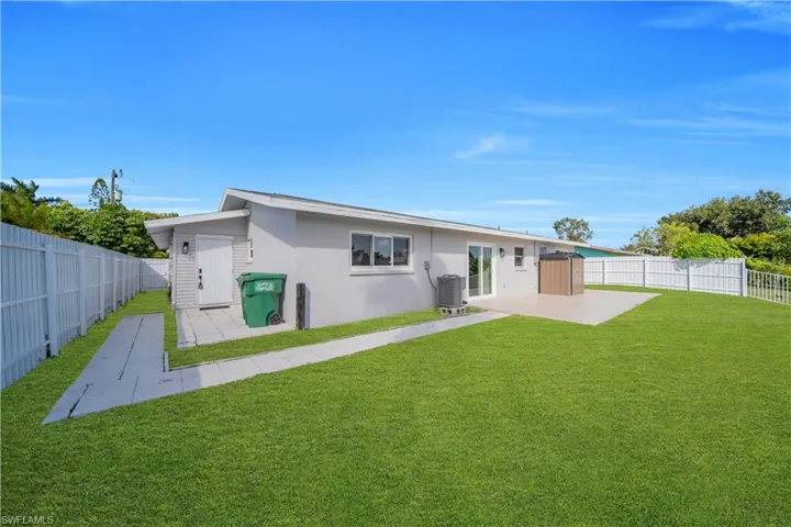 Rear exterior featuring a concrete patio, white vinyl fencing, and a manicured lawn