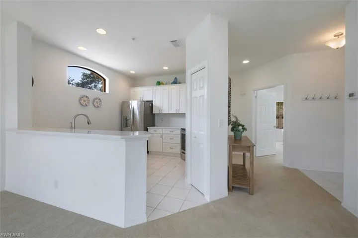 Kitchen featuring light tile patterned floors, light carpet, white cabinets, stainless steel appliances, and recessed lighting