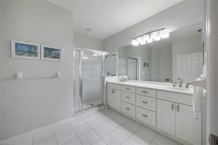 Full bath with double vanity, light tile patterned floors, and a shower stall