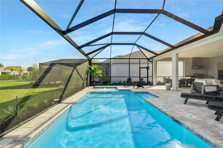Outdoor pool featuring a sunroom, a patio area, glass enclosure, a lawn, and grilling area