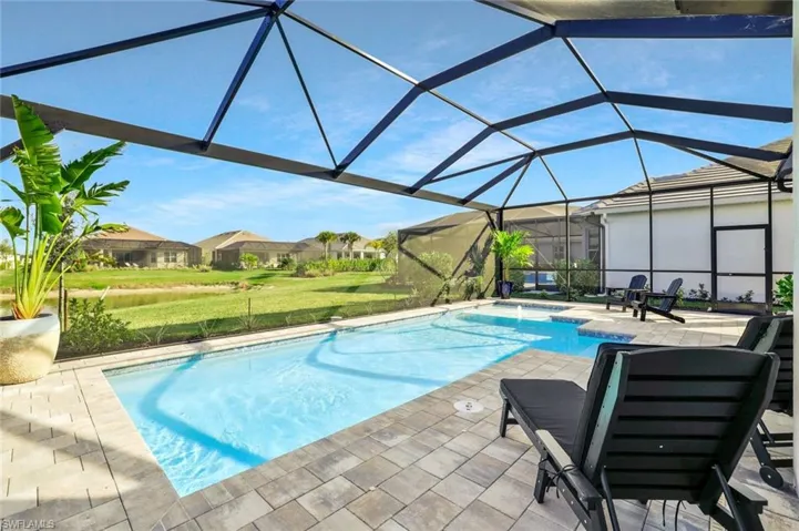 Outdoor pool featuring a sunroom, a patio, glass enclosure, a lawn, and a residential view