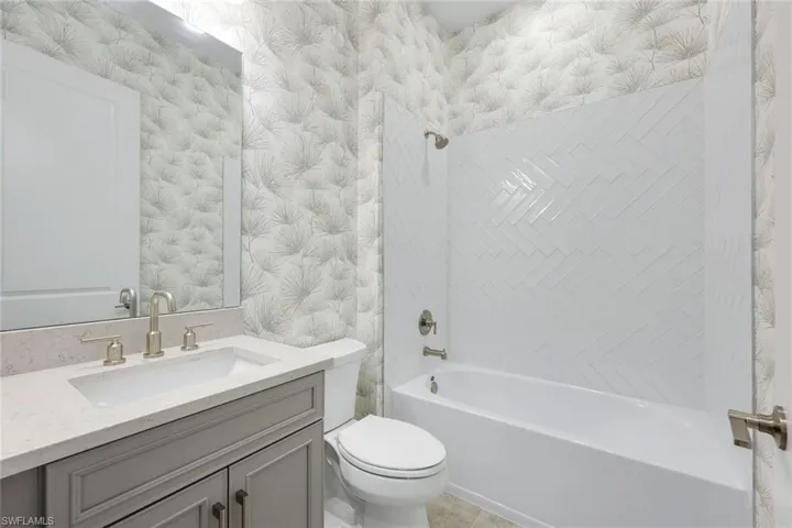 Bathroom with wallpapered walls, vanity, and shower / bathtub combination