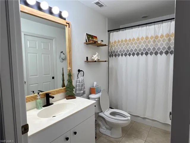 Bathroom featuring a white vanity with an integrated sink, a dark single-handle faucet, and a framed mirror with overhead vanity lighting
