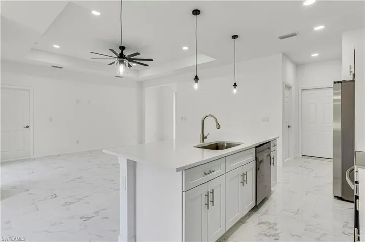 Kitchen with a raised ceiling, an island with sink, ceiling fan, and sink