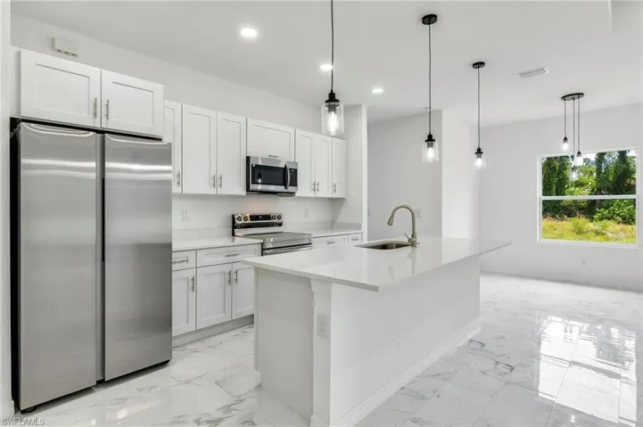 Kitchen featuring an island with sink, stainless steel appliances, decorative light fixtures, sink, and white cabinetry