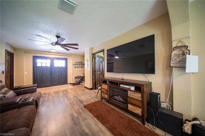 Living room featuring a textured ceiling, wood finished floors, a glass covered fireplace, and a ceiling fan