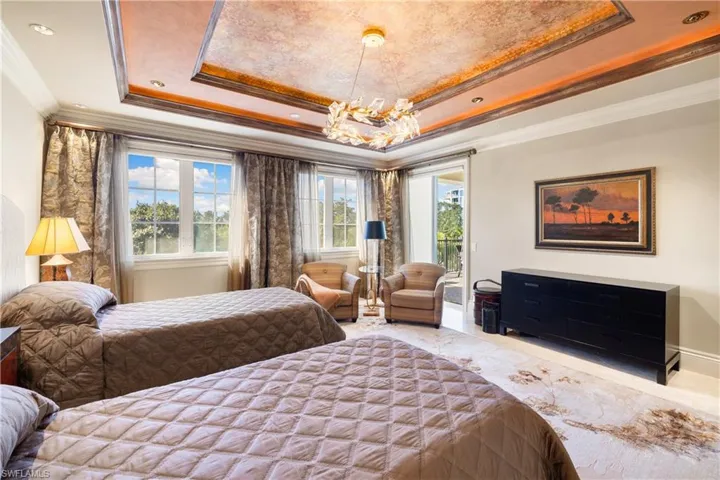 Recessed tray ceiling with integrated lighting, chandelier, multiple windows with transom panes, and light-toned flooring