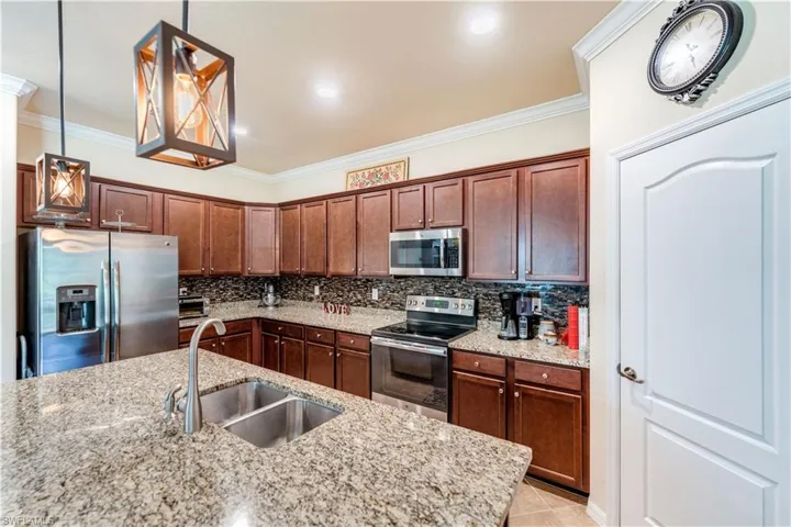 Kitchen with stainless steel appliances, sink, decorative light fixtures, decorative backsplash, and light tile patterned flooring