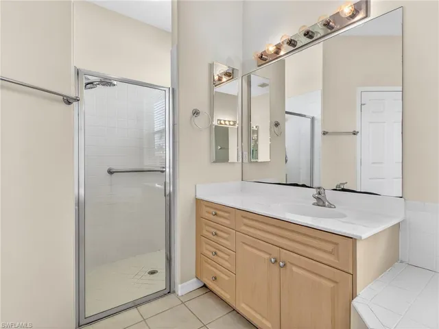 Bathroom with a glass-enclosed shower featuring white tile, a light wood-finish vanity with a single sink, an integrated countertop, and an expansive wall mirror