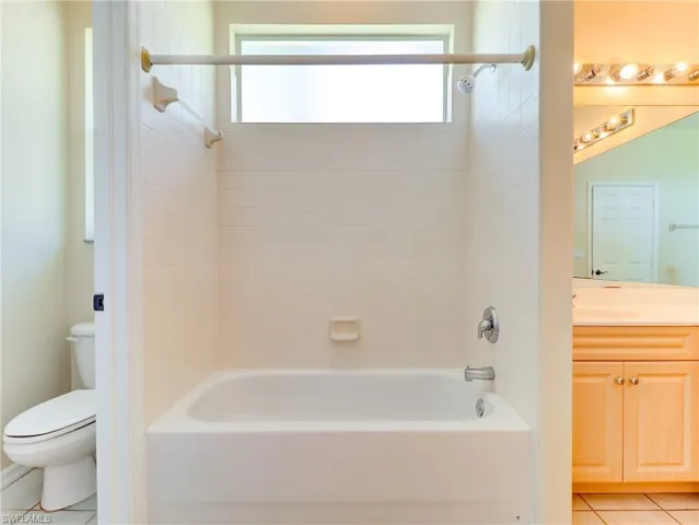 Bathtub with off white  tile surround, featuring a chrome shower fixture and an transom window