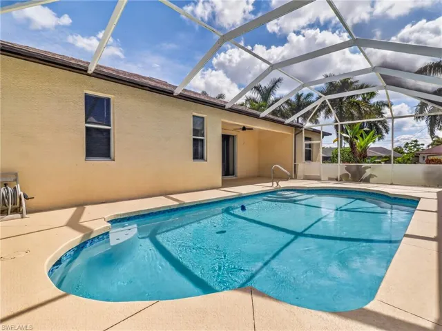Screened-in outdoor pool featuring a textured concrete pool deck, integrated steps, and a handrail