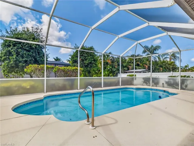 Screened swimming pool enclosure featuring a kidney-shaped pool with blue tile trim, a stainless steel handrail, and a spacious surrounding deck