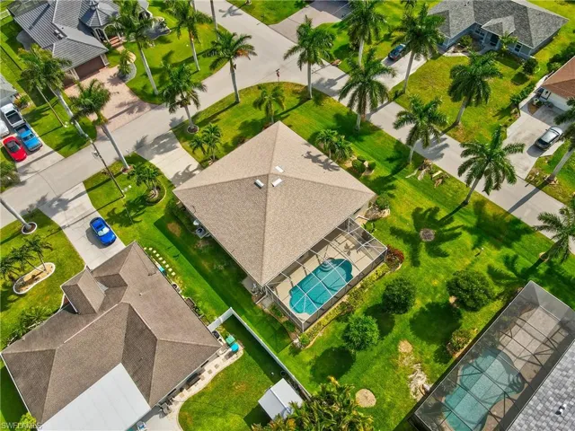 Property featuring a private screened-in swimming pool, a well-maintained lawn, mature palm trees, and a spacious paved driveway