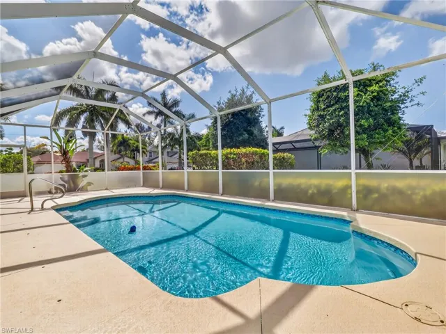 Screened outdoor pool area featuring a freeform pool with integrated steps, a surrounding concrete deck, and a safety handrail