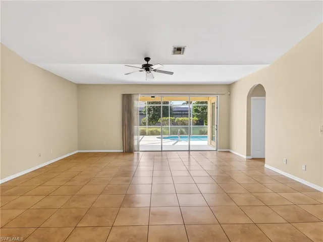Spacious interior room featuring floor tiles, direct access to the outdoor pool area through sliding glass doors, a ceiling fan, and an arched doorway