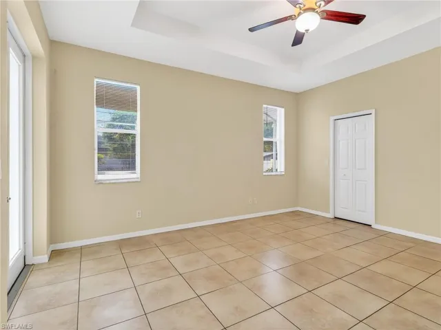 Spacious room featuring tray ceiling with ceiling fan, ceramic tile flooring, and multiple windows with blinds