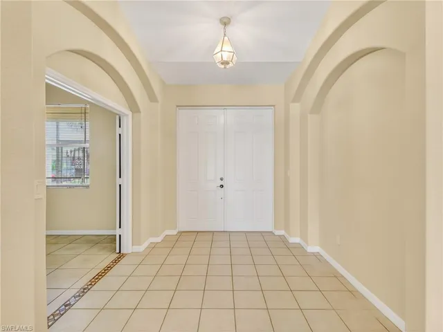 Entryway featuring double panel doors, neutral tile flooring  arched wall accents, and an overhead pendant light