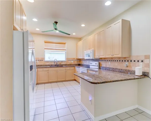 Kitchen featuring light-toned cabinetry, granite-finish countertops, and a tiled backsplash with decorative accents