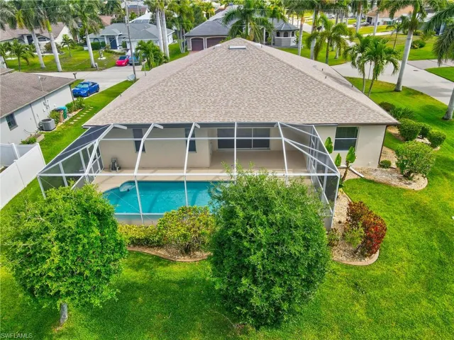 Property exterior featuring a screened-in pool, covered patio, manicured lawn, and mature landscaping