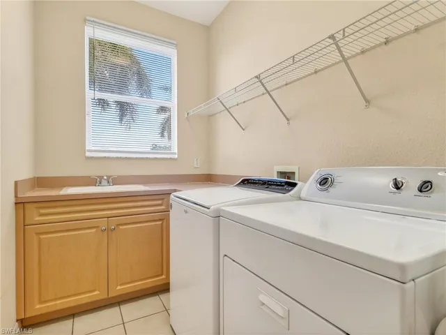 Utility room featuring a built-in sink with a countertop, wood-finish cabinetry, wire shelving, and tile flooring