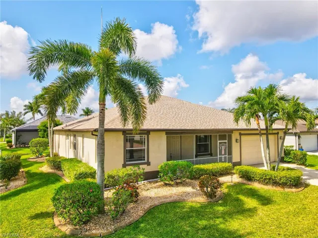 Exterior featuring a stucco facade, tan shingle roof, established palm trees, and well-maintained shrubbery