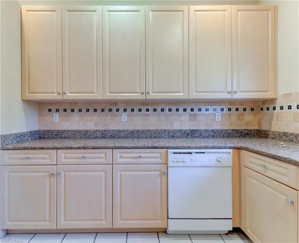 Kitchen featuring light wood-finish cabinetry, granite-style countertops, and a tile backsplash with decorative accents