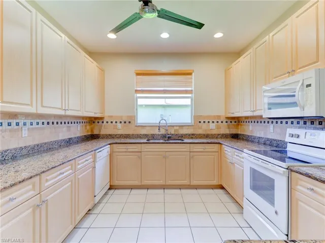 Kitchen featuring extensive light wood cabinetry, stone countertops, a decorative tile backsplash, recessed lighting, and a white tile floor