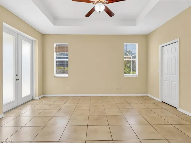 Spacious room featuring neutral wall tones, large format tile flooring, a tray ceiling, and a ceiling fan