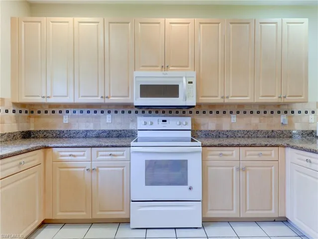 Kitchen featuring extensive light wood-finish cabinetry, speckled countertops, and a tiled backsplash with decorative accents