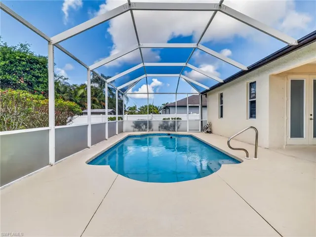 Screened enclosure featuring a freeform swimming pool with a stainless steel handrail, surrounding patio, and exterior property wall with double glass-panel doors