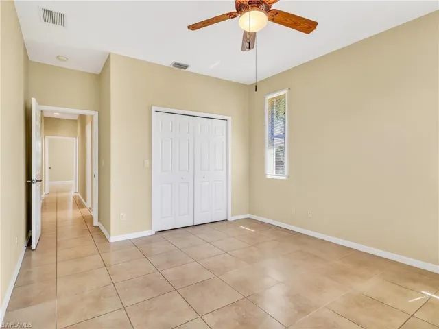 Bedroom featuring ceramic tile flooring, a ceiling fan with light fixture, bi-fold closet doors, and a vertical window
