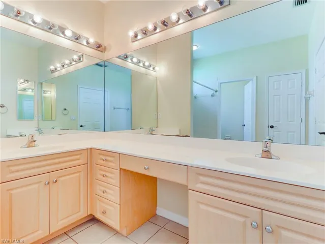 Double vanity with light finish cabinetry and integrated sinks, featuring a dedicated makeup vanity area and mirror with strip lighting