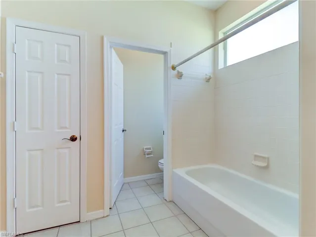 Bathroom featuring a white bathtub with subway tile surround, a high transom window, and light-toned tile flooring